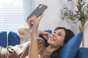 Young woman relaxing on sofa using smartphone at home