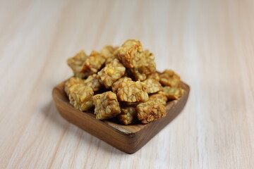 Fried tempeh in small cubes in a square teak bowl.