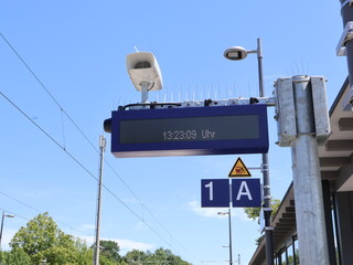 Digital Display Showing Time at an Outdoor Railway Station Platform. Digital information display at a train station with a visible platform sign under a clear blue sky.