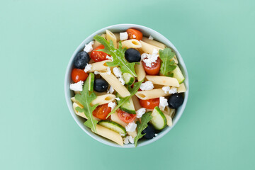Mediterranean Pasta Salad in bowl with Fresh Vegetables and Herbs on green background. Top view