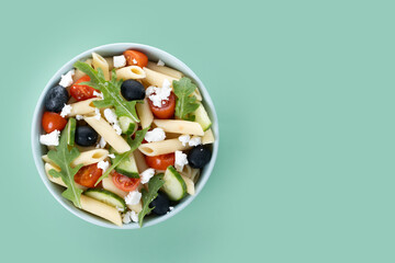 Mediterranean Pasta Salad in bowl with Fresh Vegetables and Herbs on green background. Top view. Copy space