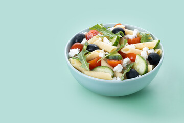 Mediterranean Pasta Salad in bowl with Fresh Vegetables and Herbs on green background. Copy space