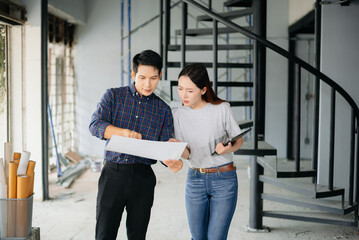 Asian architects collaborating with floor plans, tablet, and building models at a modern construction site.