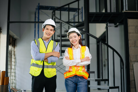 Asian engineers in safety vests and hard hats smiling on a construction site. Teamwork, pride, and professionalism in architecture