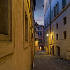 Twilight casts a warm glow over the narrow alleys of Siena,  where historic stone buildings and elegant facades create an atmospheric and timeless urban scene. Travel to Tuscany, Italy.