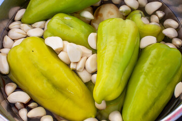 Fresh green bell peppers and peeled garlic cloves soaking in water, ready for pickling or cooking