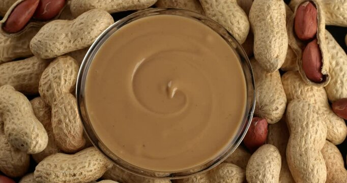 Glass bowl with creamy peanut butter on a background of peanuts. Close-up footage on the rotating table.
