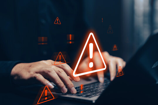 Digital cybersecurity alert with glowing orange warning signs overlaying a person's hands holding a smartphone and laptop in a dark, tech-focused environment.
