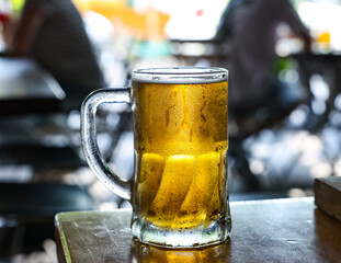 Image of a cold beer mug. The mug is of clear glass, highlighting the golden and bright color of the beer.