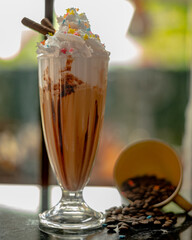 creamy ice cold frappe with whipped cream on top with sprinkles on top and coffee beans in the background. 