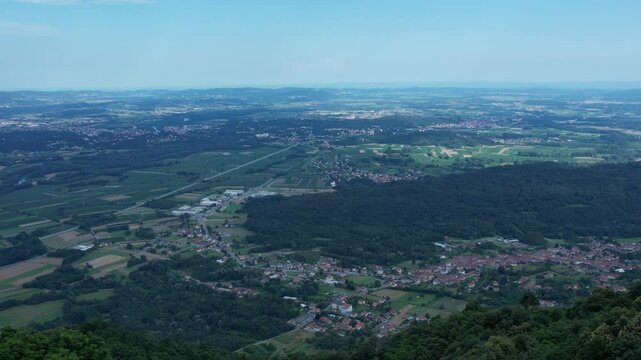 Drone panorama of the Ivrea Morainic Amphitheatre seen from Brosso, Val Chiusella, Italy, showing lush green plains, woods, and scattered villages under clear sky, high drone shot, slow motion