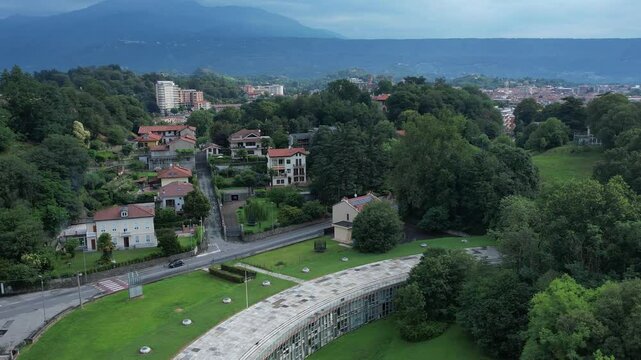 Talponia, the semi-subterranean residential unit in Ivrea, Piedmont, designed by Gabetti Isola in 1968, set in a curved green park at the city forest edge, drone pull away shot slow motion, Italy