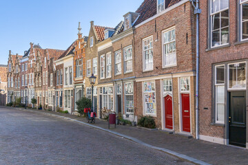 This captivating photo showcases a charming, historic street in Dordrecht, Netherlands, lined with classic Dutch gabled houses on a sunlit cobblestone path. Dordrecht, Netherlands. 16 March 2025.