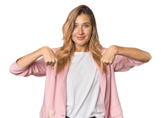 Young blonde in stylish pink suit points down with fingers, positive feeling.