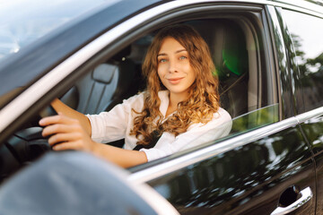 Beautiful woman driving a car in a white camisole is looking out the window. Young woman is driving...