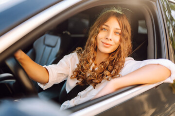 Beautiful woman driving a car in a white camisole is looking out the window. Young woman is driving...