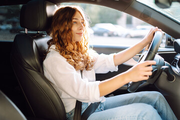 Beautiful woman driving a car in a white camisole is looking out the window. Young woman is driving...