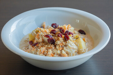  delicious and healthy oatmeal served in a white bowl. The oatmeal is topped with grated carrots, fresh apple slices, and dried red cranberries