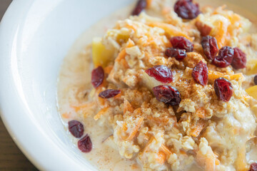  delicious and healthy oatmeal served in a white bowl. The oatmeal is topped with grated carrots, fresh apple slices, and dried red cranberries