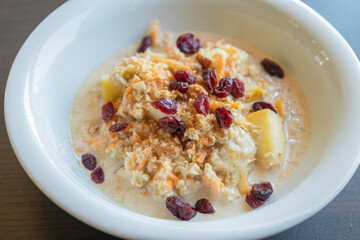  delicious and healthy oatmeal served in a white bowl. The oatmeal is topped with grated carrots, fresh apple slices, and dried red cranberries