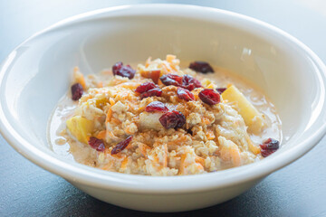  delicious and healthy oatmeal served in a white bowl. The oatmeal is topped with grated carrots, fresh apple slices, and dried red cranberries