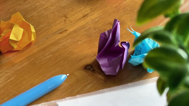 Multi-colored crumpled post-it notes fall one by one into a pile on the table. Symbol of creative disorder, reworking of ideas and rejection of the superfluous. Close-up.