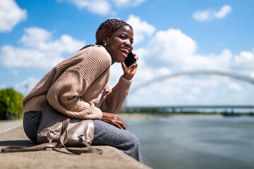 Young cheerful black woman is talking on the phone. She is laughing and enjoying sunny day in the...