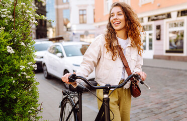 Cheerful woman with bicycle on sunny city street enjoying a walk. Tourist with bicycle walking in...