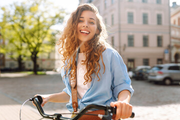 Cheerful woman with bicycle on sunny city street enjoying a walk. Tourist with bicycle walking in...