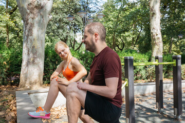 Fit couple stretching legs in a park during workout. Healthy lifestyle, fitness, and exercising outdoors. Man and woman doing warm-up exercises before training. Active people enjoying sunny day.