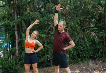Active young couple stretching outdoors before a workout. Man and woman doing warm-up exercises in a park. Healthy lifestyle concept.