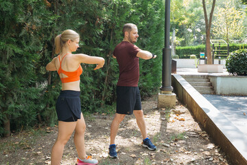 Active couple warming up before a workout.  They perform stretching exercises in a park. Healthy lifestyle concept.
