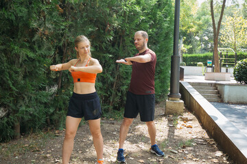 Young athletic couple warming up together in a park. Man and woman doing arm stretches before fitness workout. Healthy lifestyle concept.