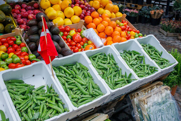 Different fruits and vegetables well organized and presented on food market in Denmark. Fresh green peas, tomatoes, avocado, onions and oranges in boxes. Danish flag as a symbol of local products.