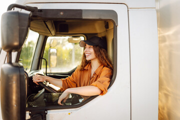 A young female driver in a reflective vest sits behind the wheel of a large truck. A woman in a cap...
