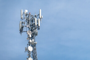A telecommunications tower, bristling with antennas and dishes against a clear sky, symbolizes...
