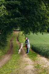 Obraz premium Person interacting with a playful dog on a scenic dirt path surrounded by lush greenery and trees, showcasing a joyful moment in nature with a sense of companionship and tranquility