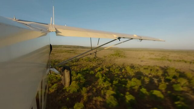 Hyperlapse of aerial wide small plane taking off and flying over savannah with scattered shrubs and waterbody with sunrise in Kenya