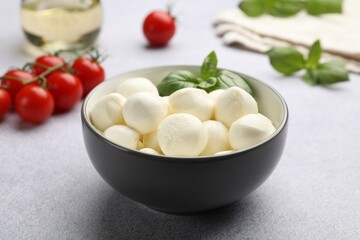 Tasty mozzarella cheese balls, tomatoes and basil on light grey table, closeup