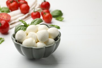 Tasty mozzarella cheese balls, tomatoes and basil on white wooden table, closeup. Space for text