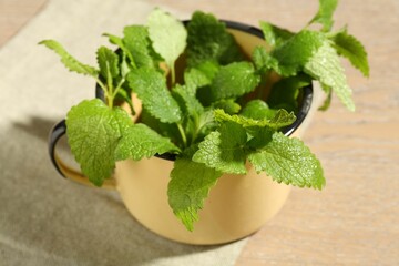 Fresh lemon balm leaves in mug on wooden table, closeup