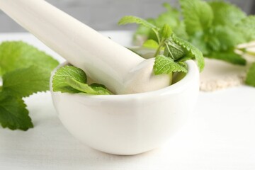 Fresh lemon balm leaves and pestle in mortar on white wooden table, closeup