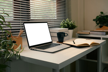 Modern workspace with blank laptop screen, notebook, and coffee mug in a bright room