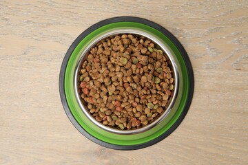 Dry pet food in feeding bowl on wooden background, top view