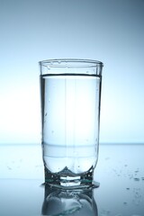 Fresh water in glass on mirror table against light blue gradient background, closeup