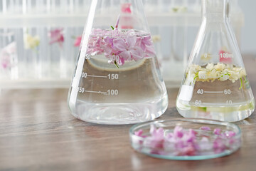 Making luxury perfume. Essential oils in glassware and flowers on light wooden table, closeup