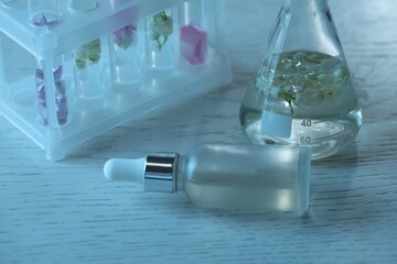 Making luxury perfume. Essential oils in glassware and flowers on white wooden table, closeup