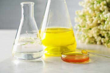 Making luxury perfume. Essential oils in glassware and flowers on white wooden table, closeup