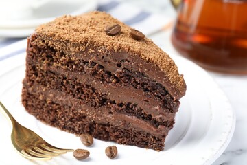 Piece of delicious chocolate cake with coffee beans and fork on white table, closeup