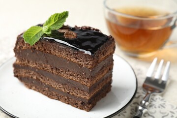 Piece of chocolate cake served with mint, fork and tea on table, closeup